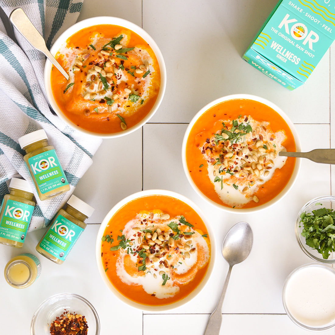 carrot ginger soup in bowls on white kitchen counter with kor shots wellness